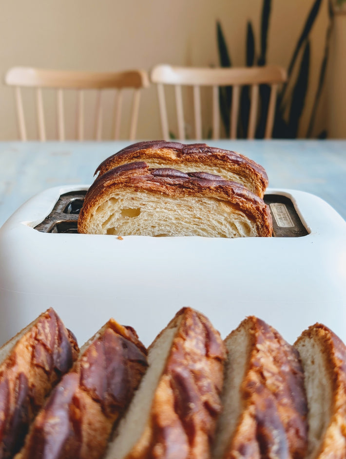 Toaster with Croissant Loaf slices, set on a table with wooden chairs in the background.