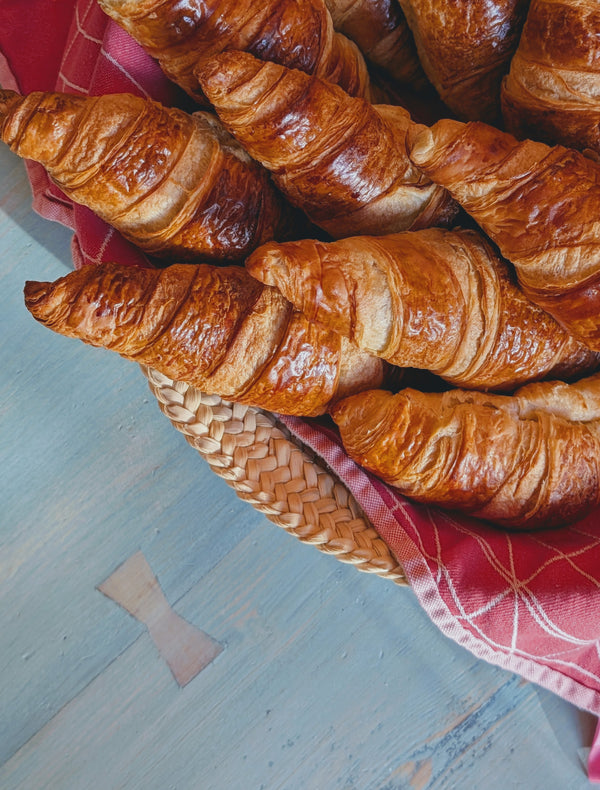 Top down view of sourdough croissants in a woven basket showcasing flaky golden layers on blue wooden table with a red napkin