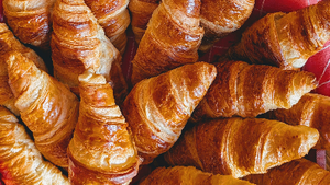 Freshly baked golden croissants with flaky layers, stacked closely on a tray