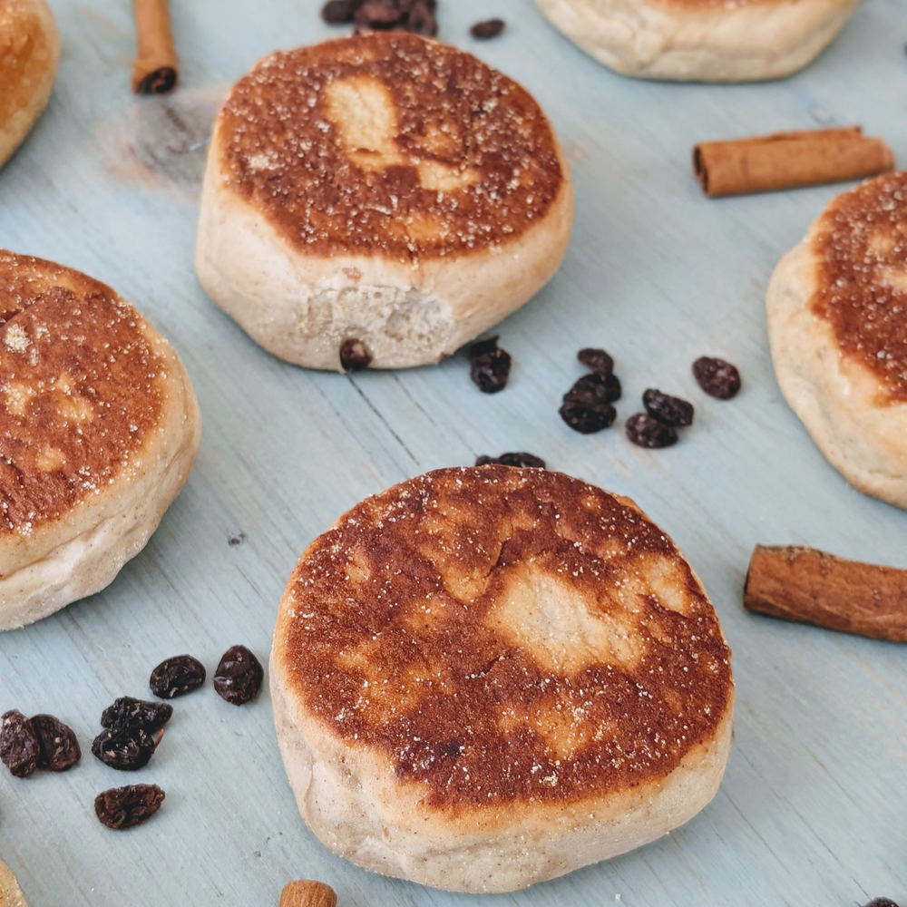 Toasted crumpets with currants scattered and cinnamon sticks on a light blue wooden board