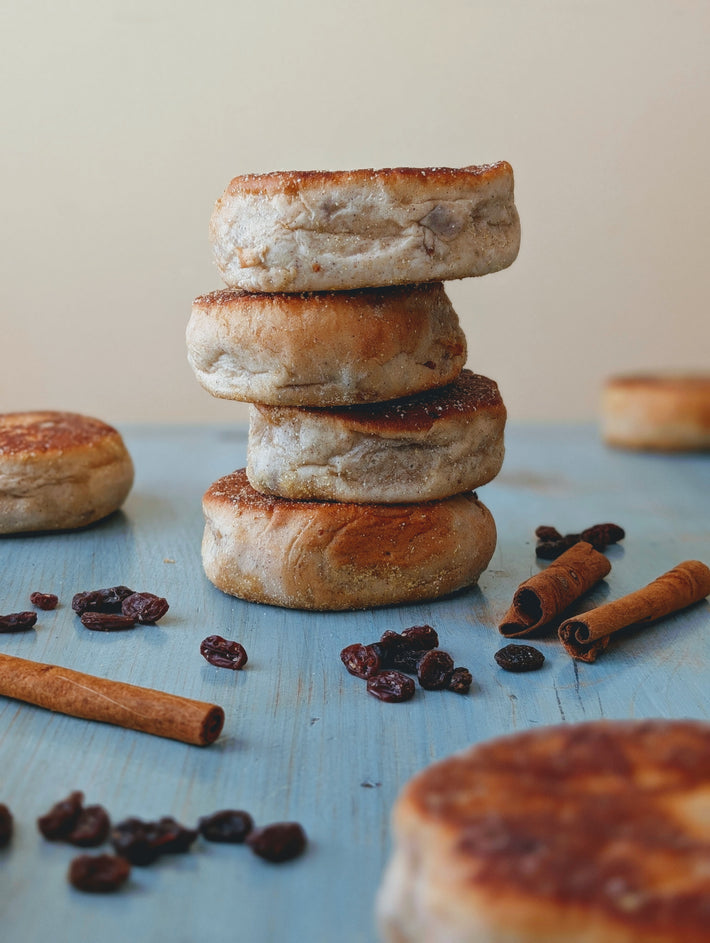Stack of four toasted English muffins on a blue wooden surface with scattered raisins and cinnamon sticks