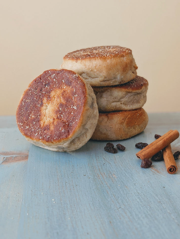 Stack of toasted English muffins with cinnamon sticks and raisins on a weathered blue wooden surface.