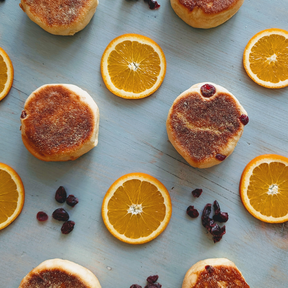Toasted small pancakes with sugar, sliced oranges and dried cranberries arranged on a blue wooden surface