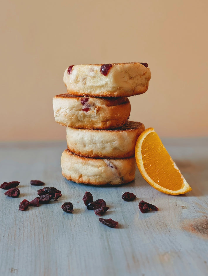 Stack of four jam-filled English muffins on a blue wooden table, scattered dried cranberries and a sliced orange wedge.