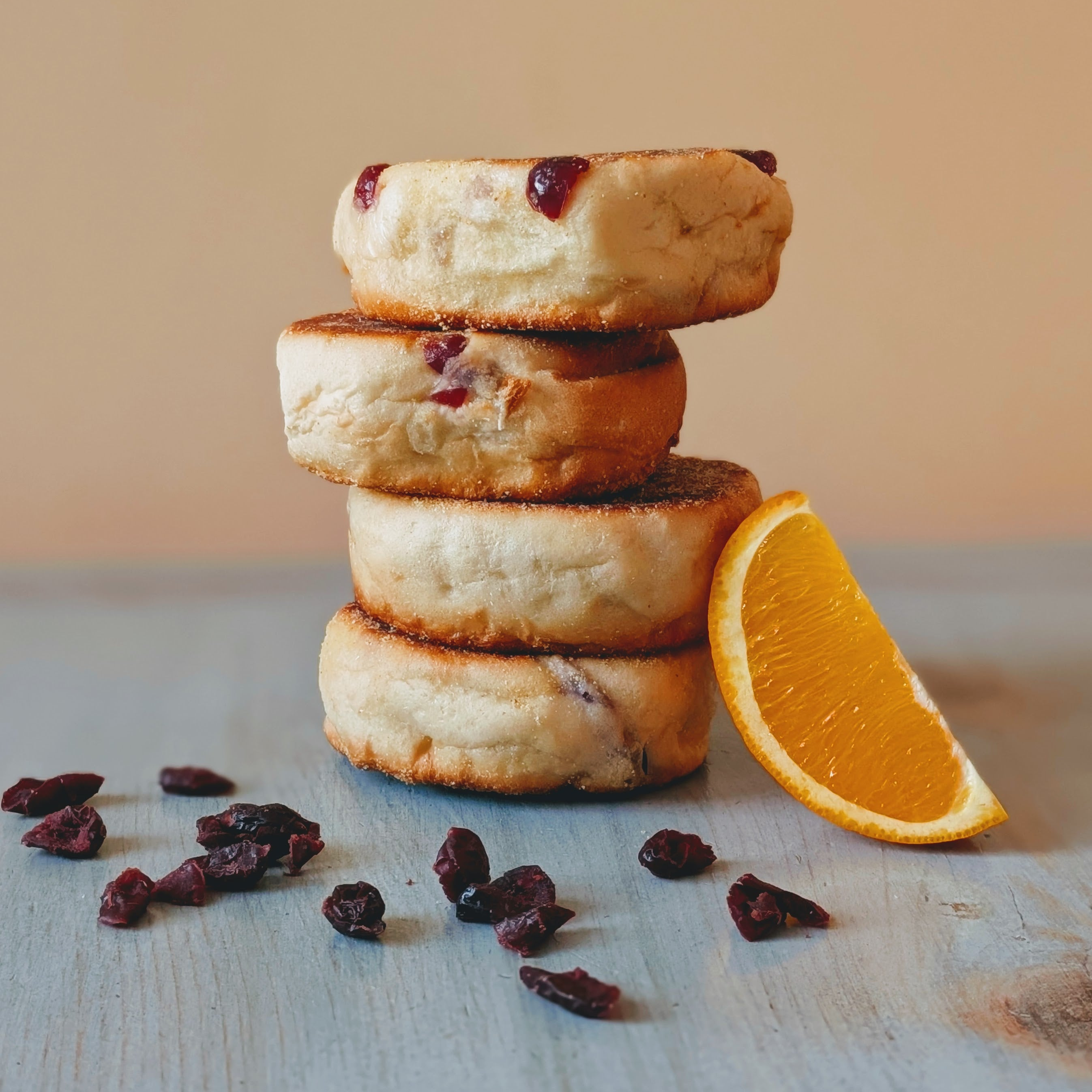 Four stacked cranberry scones with an orange wedge and scattered dried cranberries on weathered blue wood.