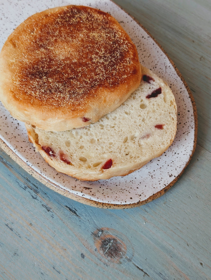 Toasted split English muffin with dried cranberry pieces on a speckled ceramic plate, on a weathered blue wooden table.