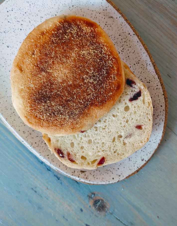Toasted cranberry English muffin halves on a speckled ceramic plate atop a blue wooden table.