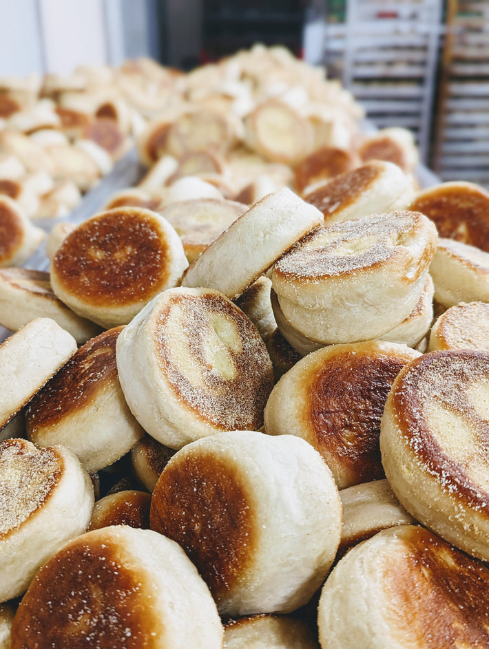Close-up of golden-brown English muffins stacked in a bakery setting.