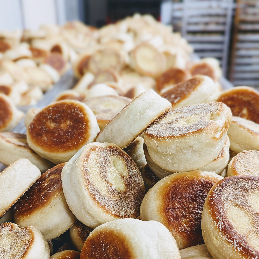 Stacked toasted English muffins with cornmeal-dusted bottoms, close-up on a bakery tray