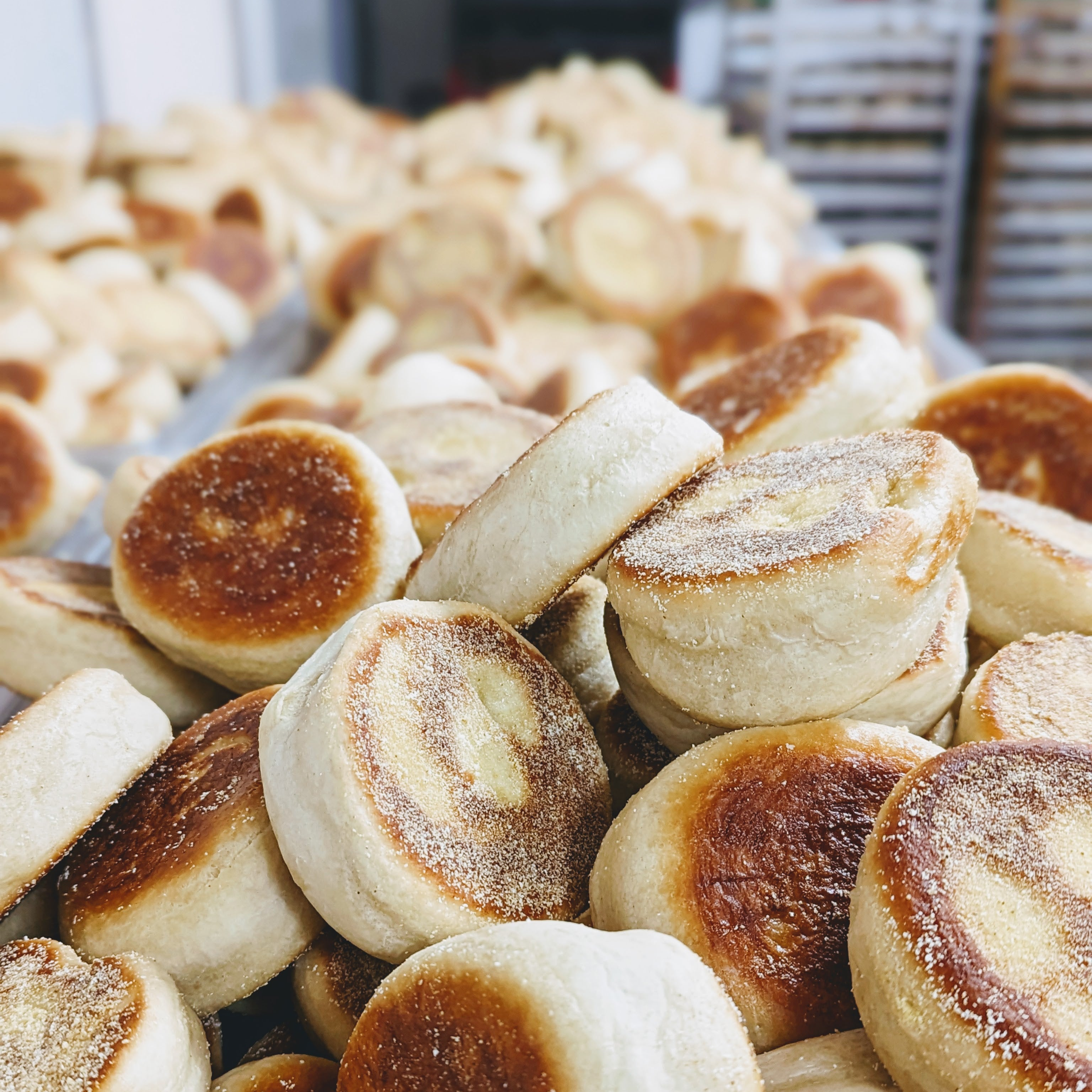Stacked toasted English muffins with cornmeal-dusted bottoms, close-up on a bakery tray