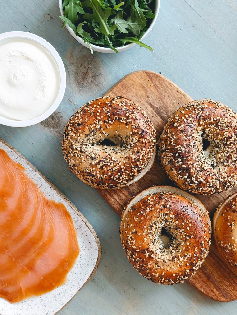Top-down view of four Everything bagels on a wooden board with smoked salmon, cream cheese, and arugula