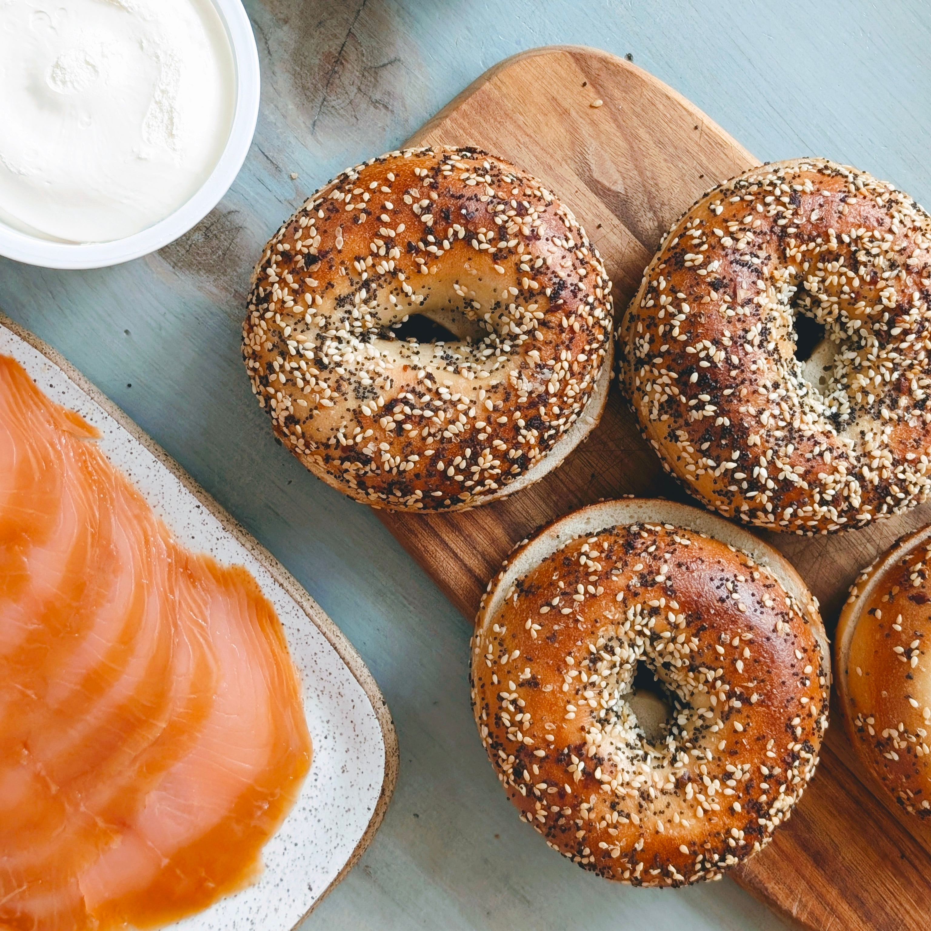 Three bagels on a wooden board with a side of salmon and arugula.