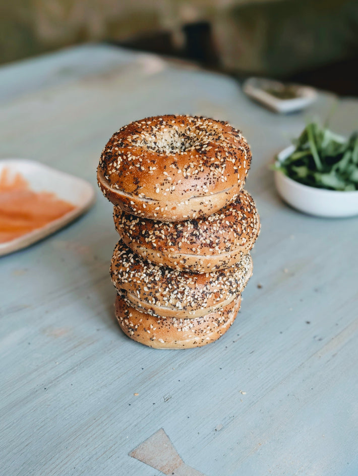 Three-quarter view of four Everything bagels stacked showcasing seeded crust on a light blue tabletop