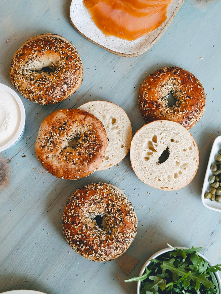 Top-down view of Everything bagels, whole and sliced, showing seeded crust on a blue board with cream cheese and salmon