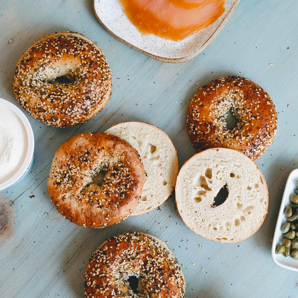 Assorted bagels on a light blue surface with spreads and toppings.