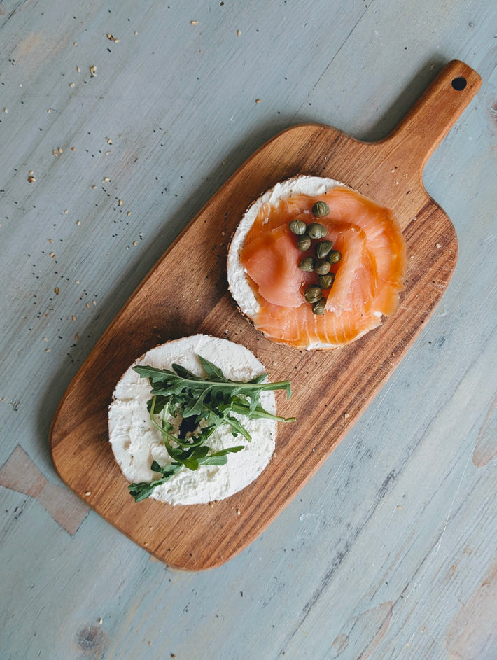 Two open-faced bagels on a wooden board with a light blue background