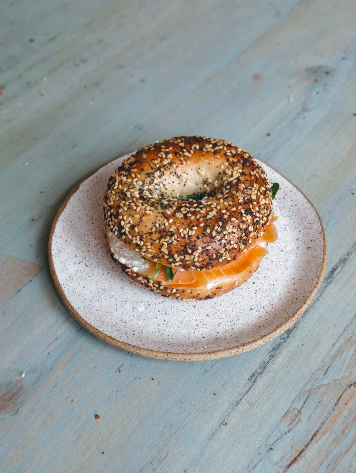 Bagel with cream cheese and salmon on a speckled ceramic plate on a wooden table.