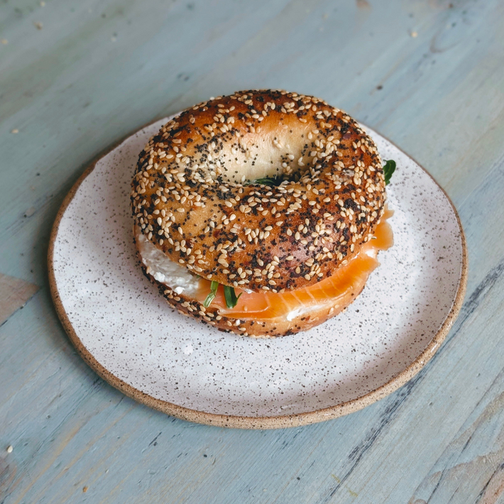 Top-down view of Everything bagel with smoked salmon and cream cheese on a speckled plate on light blue wood