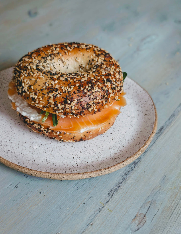 Angled view of an everything bagel sandwich showcasing smoked salmon, cream cheese, and arugula on a speckled plate over a pale blue wooden table