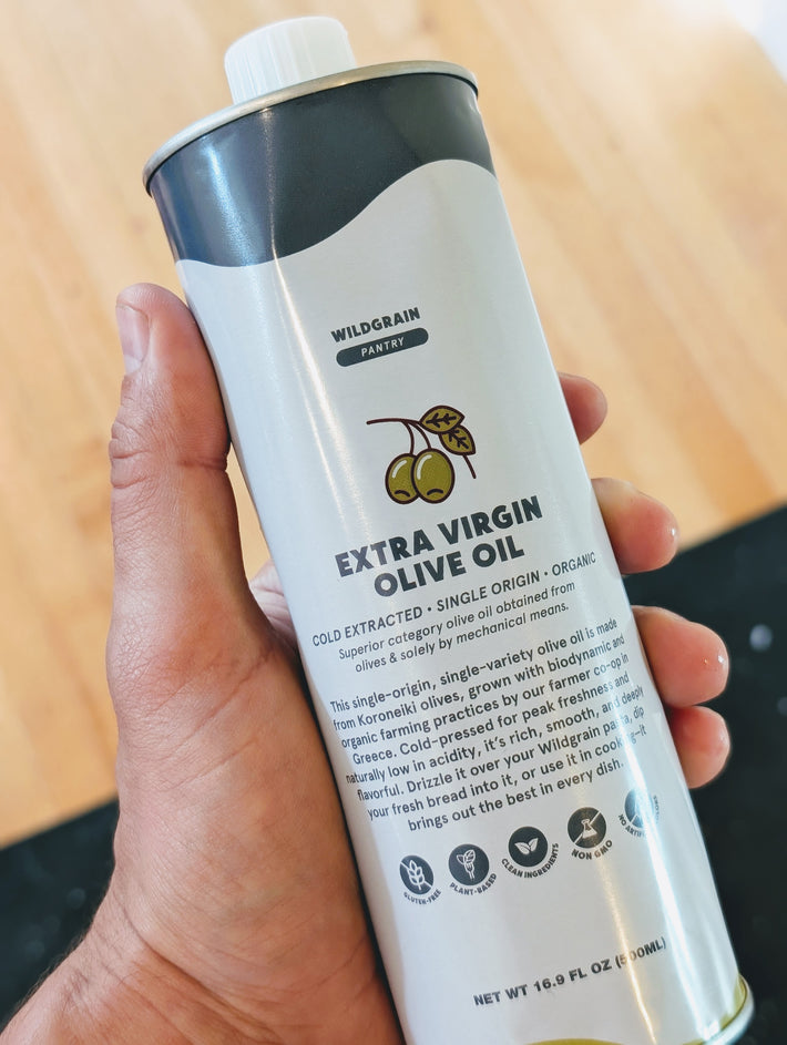 Hand holding a Wildgrain Pantry can of extra virgin olive oil with olive illustration.