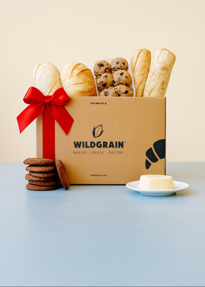 Cardboard box with bread and cookies labeled 'Wildgrain' on a light blue surface with a beige background.