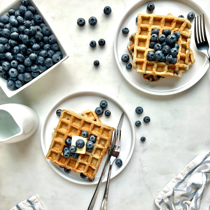 Two plates of waffles with blueberries on a marble surface.
