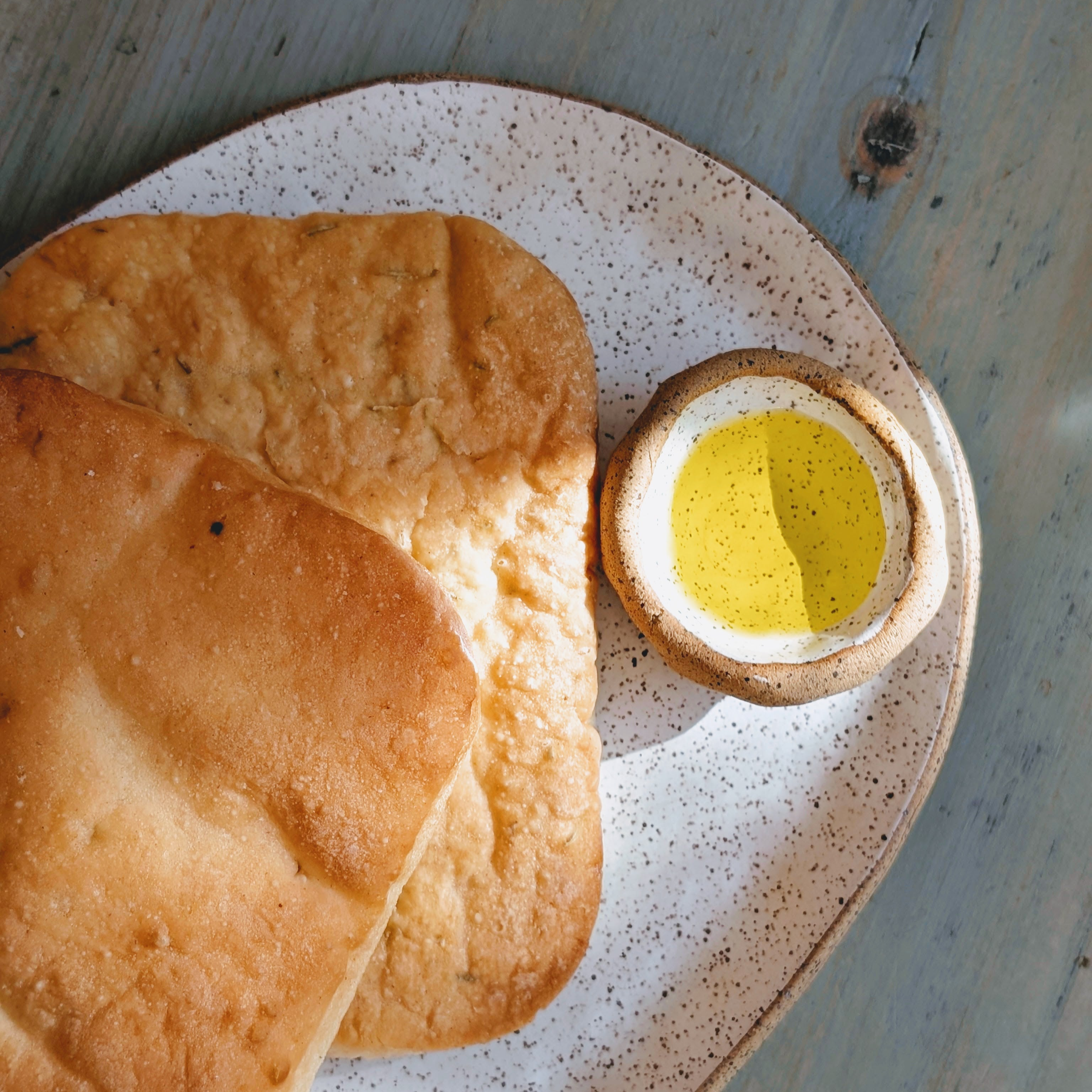 Two square flatbreads on a speckled ceramic plate with a small bowl of olive oil for dipping.