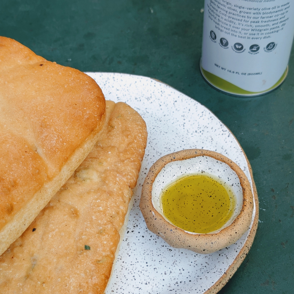 Ciabatta and herb flatbread on speckled plate with small bowl of olive oil, tin visible: NET WT 16.9 FL OZ (500ML)