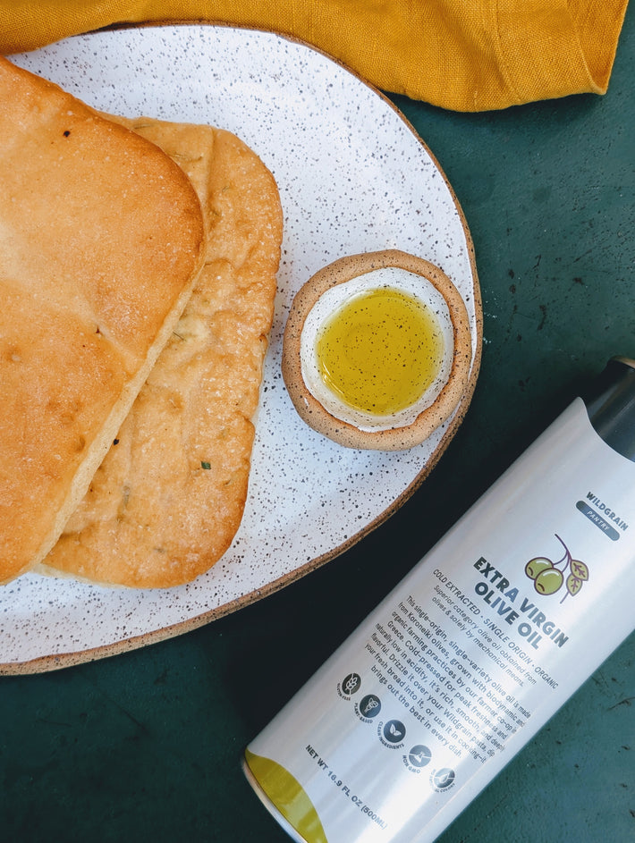 Flatbreads on speckled plate with small bowl of oil and bottle labeled 'WILDGRAIN PANTRY EXTRA VIRGIN OLIVE OIL'