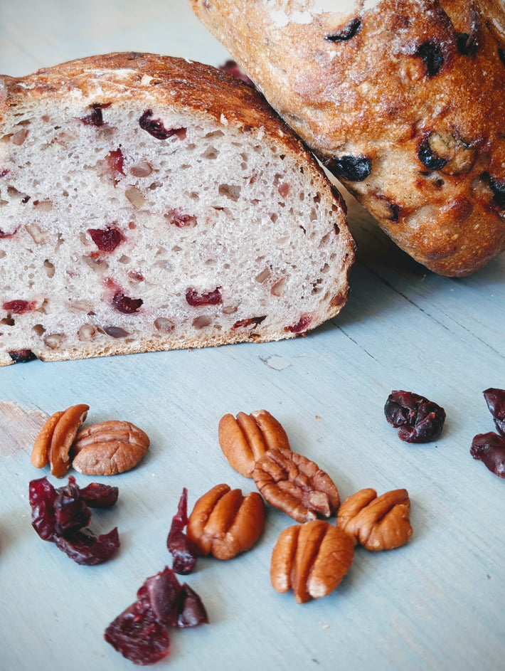 Sliced cranberry-pecan artisan bread on a pale blue wooden board with scattered pecans and dried cranberries.