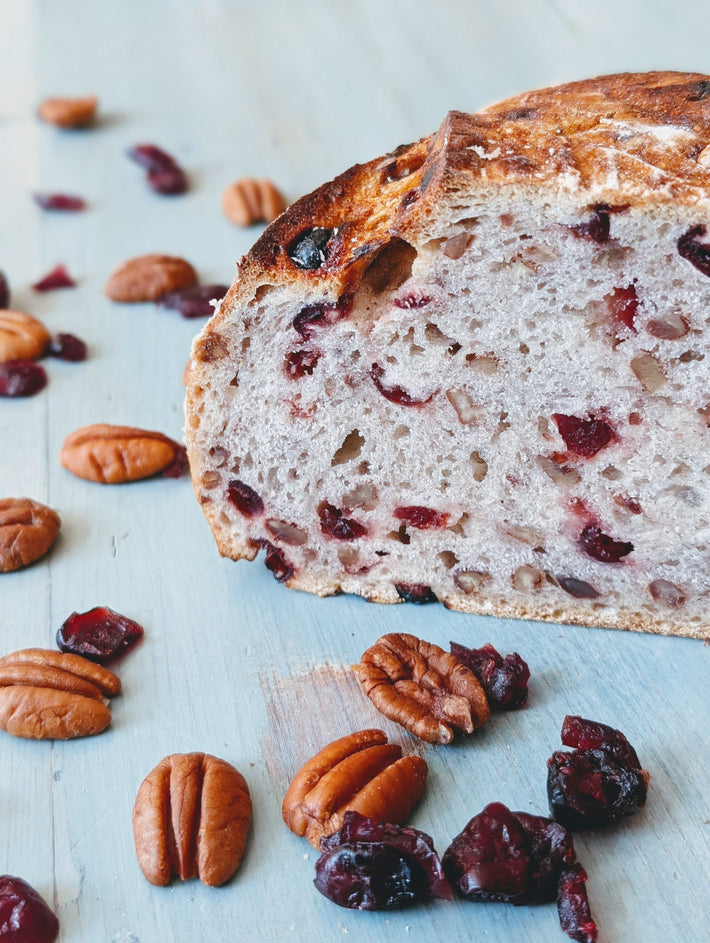 Sliced cranberry-pecan loaf on pale blue board, interior showing cranberries and chopped pecans, with scattered pecans.