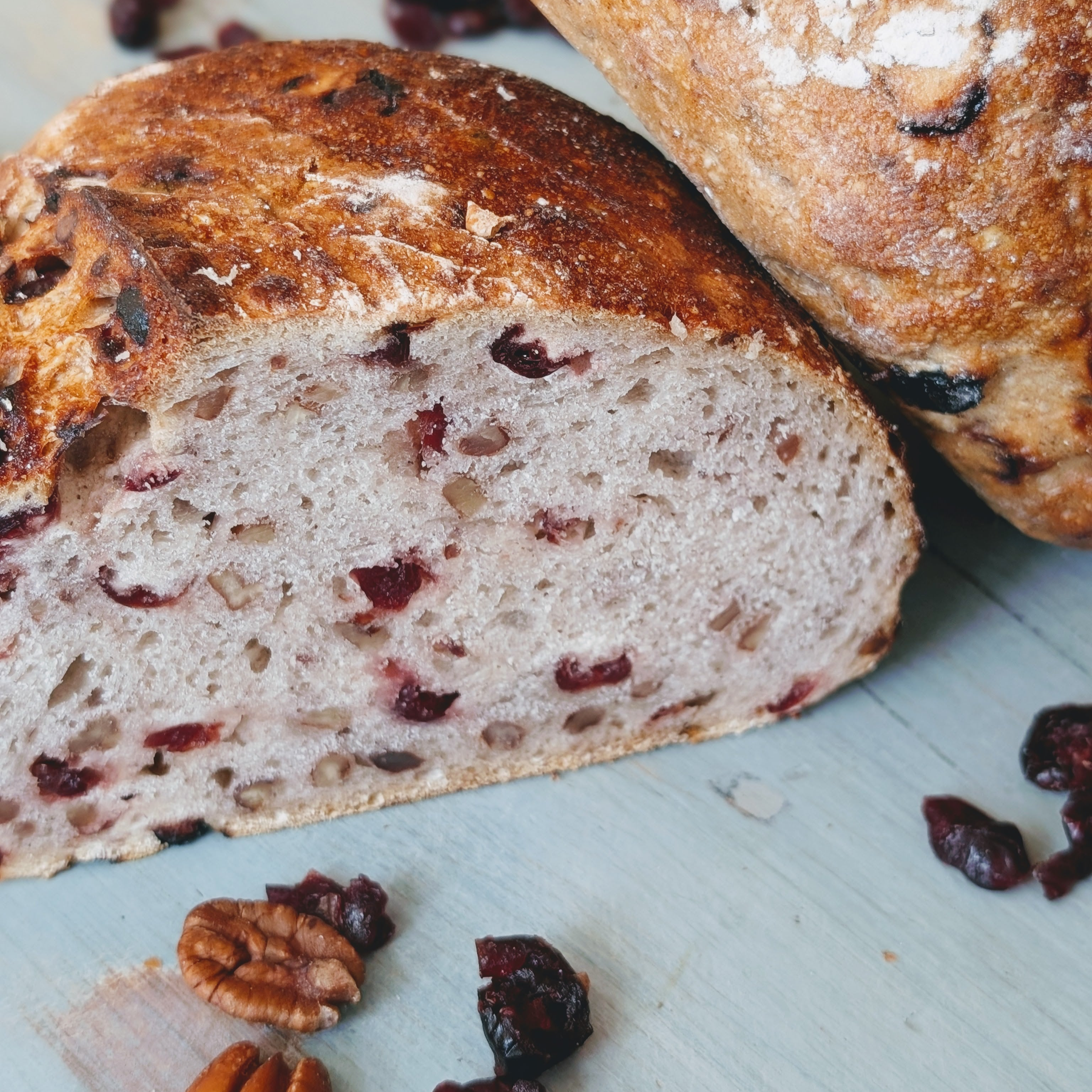 Sliced cranberry walnut artisan bread with visible cranberries and pecans on a light wooden board.