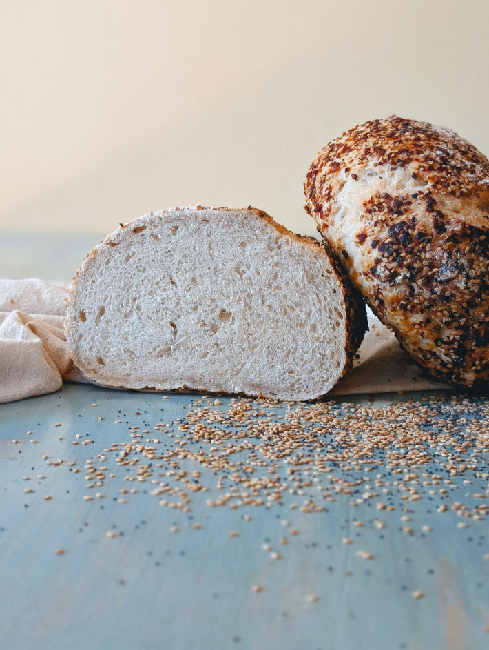 Loaf of bread with a slice cut off on a blue surface with seeds.