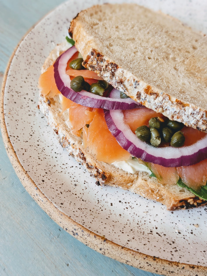 Smoked salmon sandwich with onions and capers on a speckled plate