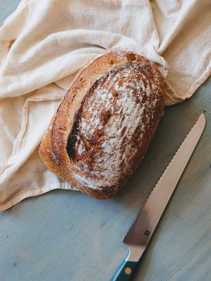 Loaf of bread on a cloth with a knife on a wooden surface