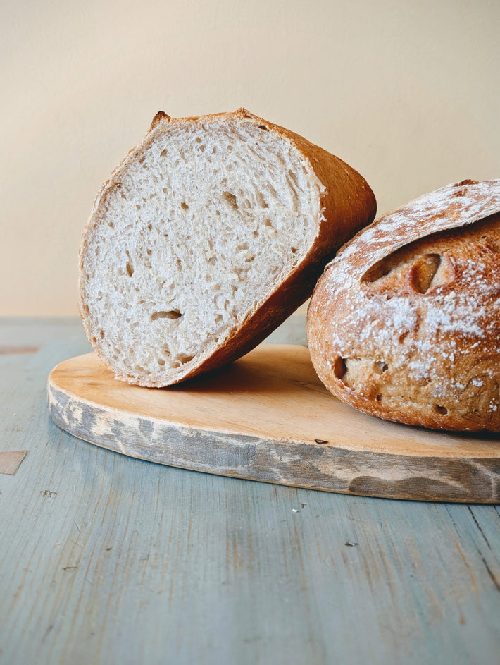 Two rustic loaves of bread on a round wooden cutting board, one sliced to show the airy crumb.