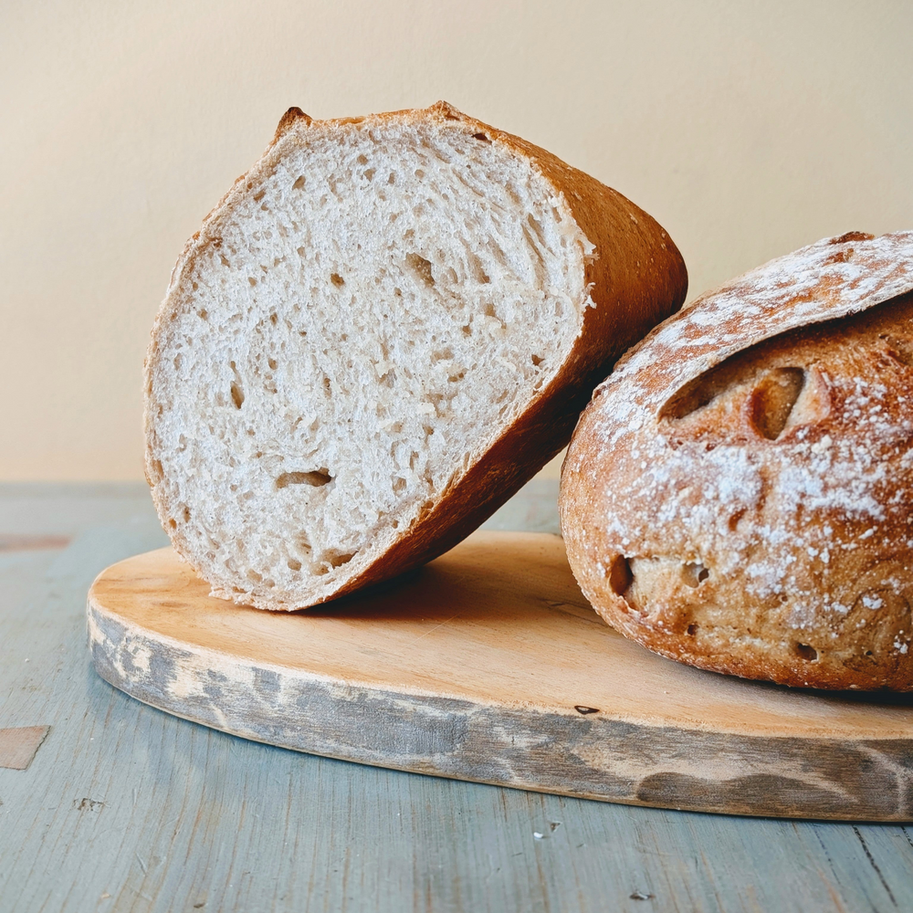 Two rustic round loaves on a worn wooden cutting board; one sliced to show the airy crumb.
