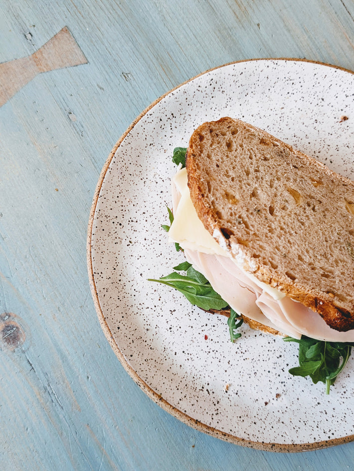 Turkey and cheese sandwich with arugula on a speckled ceramic plate on a weathered blue wooden table