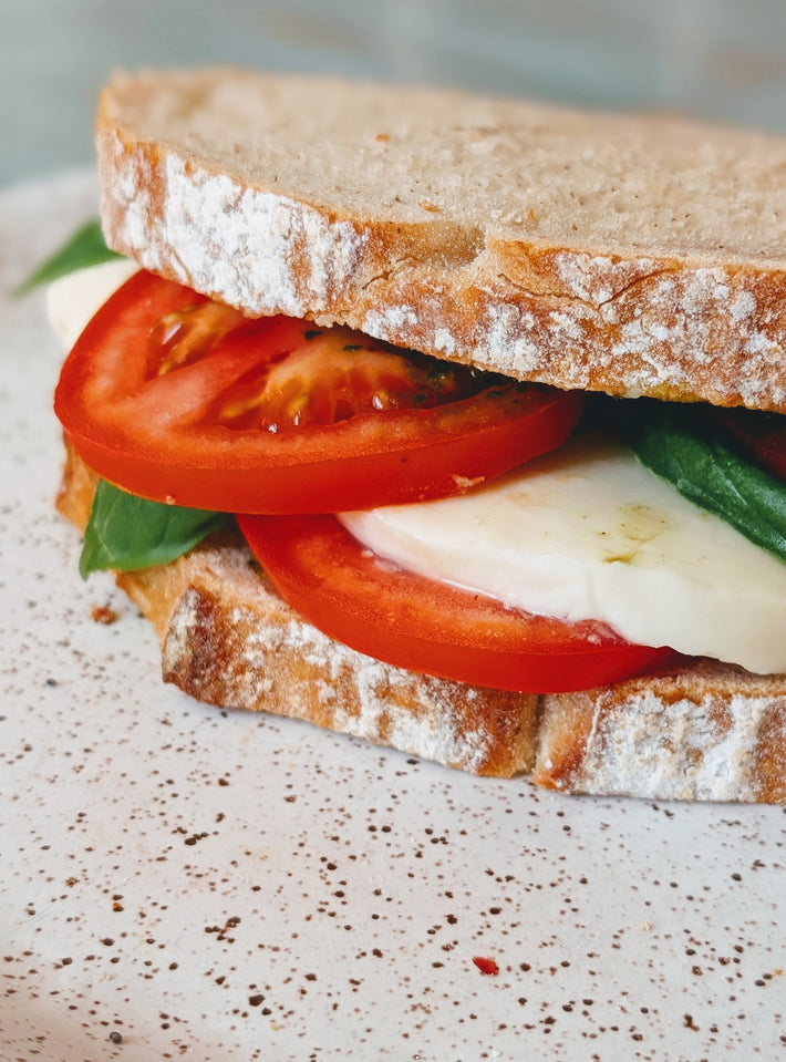 Caprese sandwich with tomato, mozzarella, and basil on a rustic bread slice.