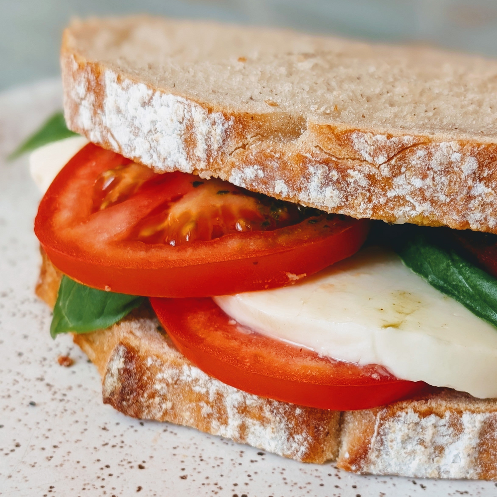 Thick-sliced rustic bread sandwich with tomato, fresh mozzarella, and basil leaves (Caprese-style)