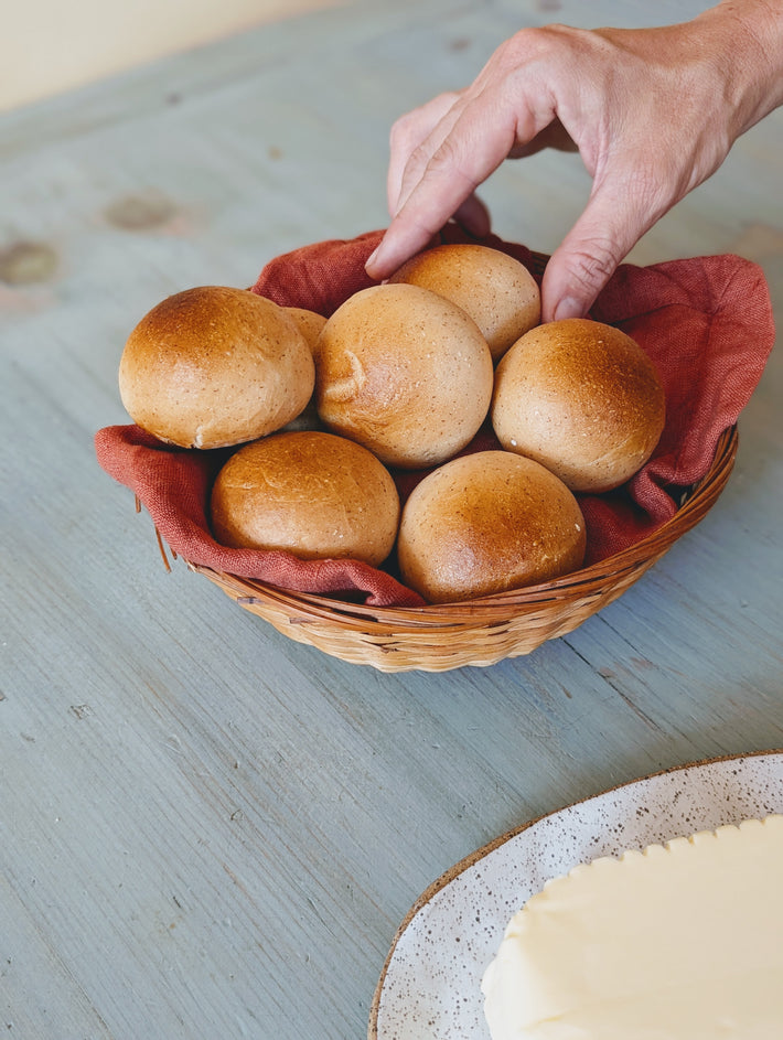 Hand reaching for a bread roll from a basket on a wooden table