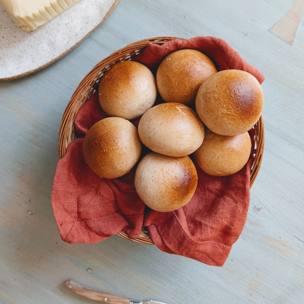 Wicker basket lined with a red cloth holding seven round golden-brown bread rolls on a pale blue table