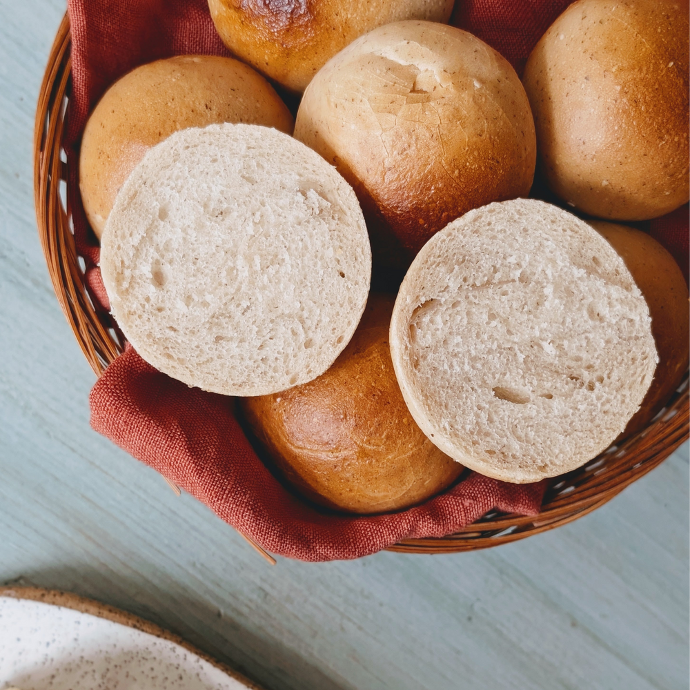 Basket of round bread rolls with two halves showing soft interior, on a red cloth liner in a wicker basket.