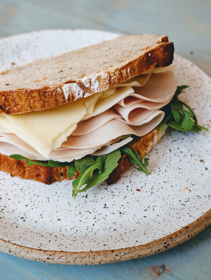 Sandwich with turkey, cheese, and arugula on a speckled plate.