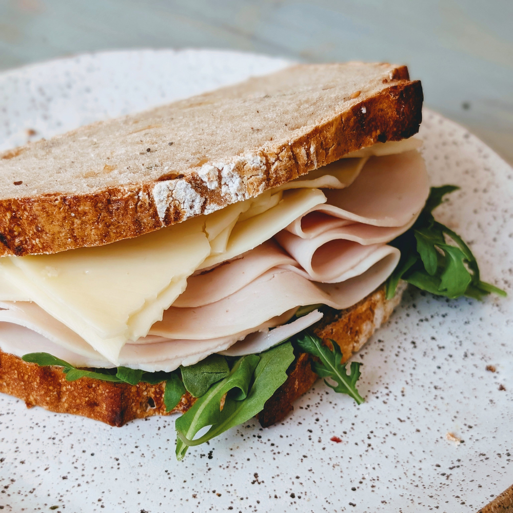 Close-up of sandwich with folded turkey, pale cheese, and arugula between crusty sourdough slices on a speckled plate