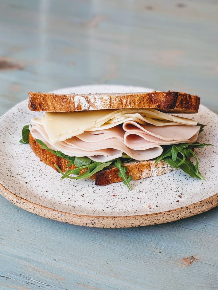 Turkey and cheese sandwich with arugula on a speckled ceramic plate.