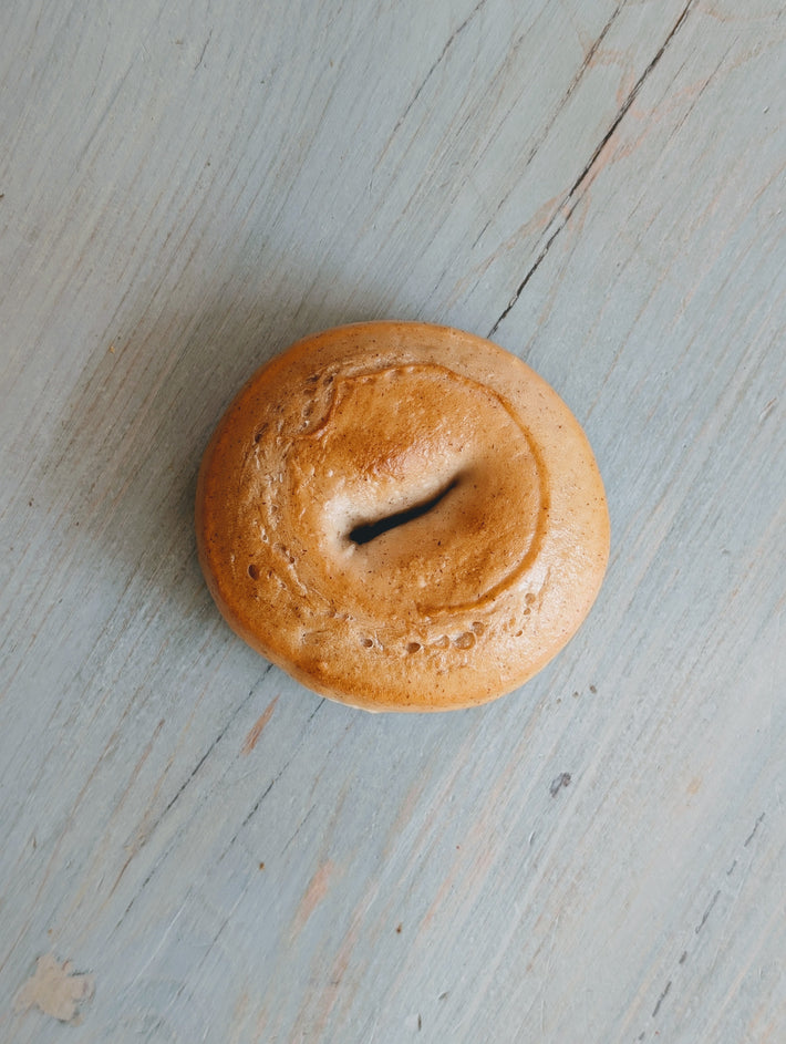 Plain bagel centered on light blue painted wooden surface.