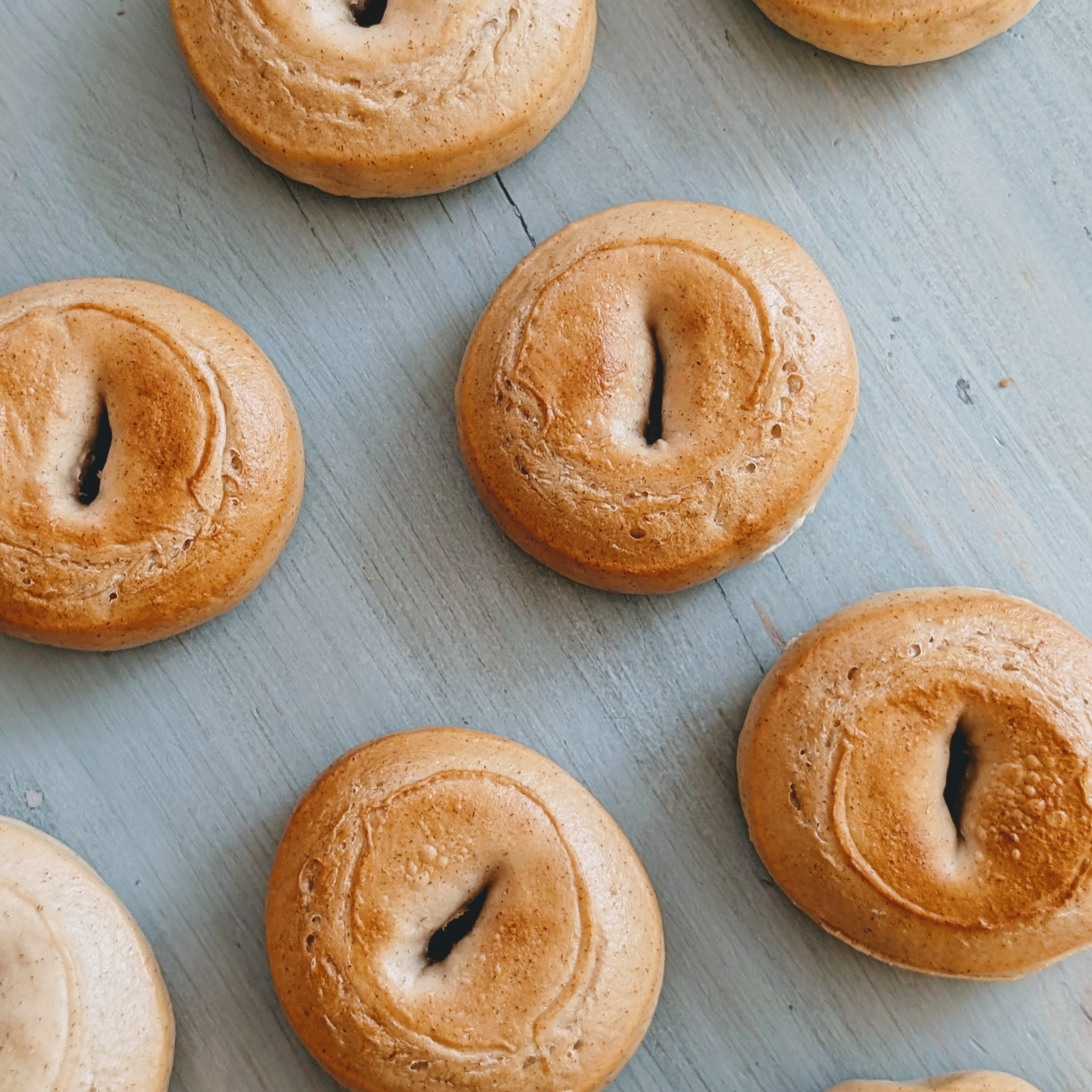 Several golden-brown bagels with small center slits arranged on a weathered blue wooden board, top view