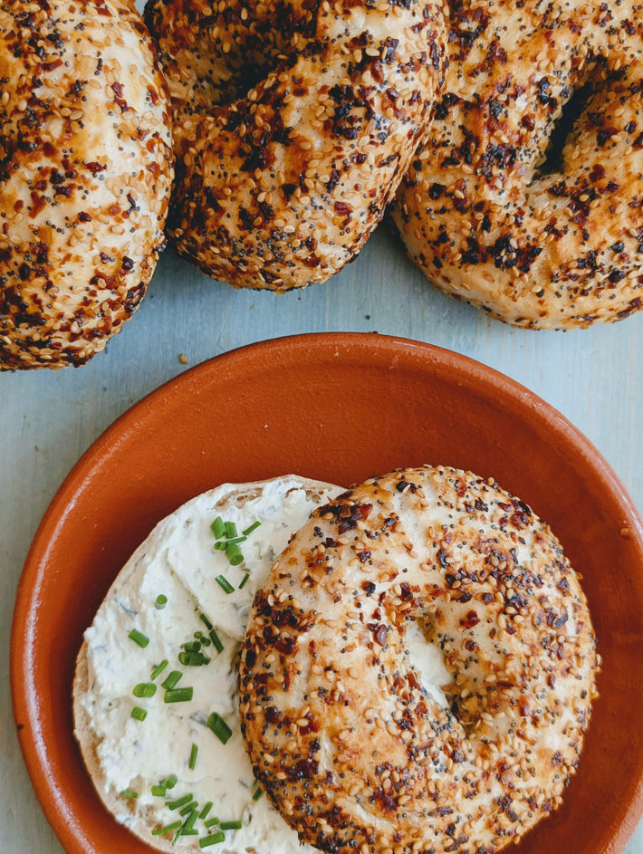 Gluten-free everything bagels with cream cheese and chopped chives on a terracotta plate, showing the bagels' golden crust and seasoning.