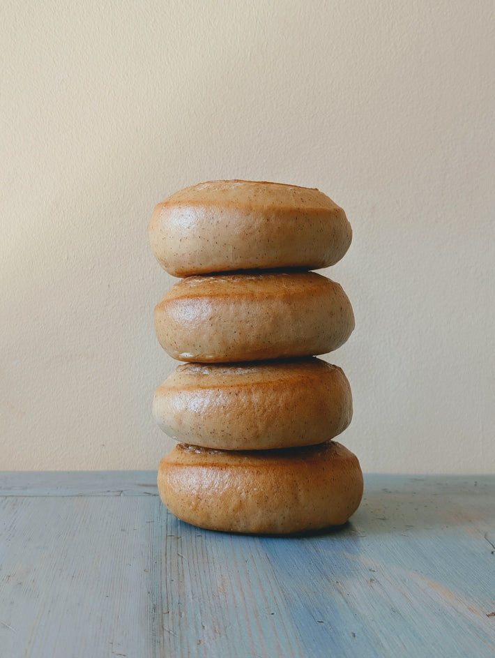 Four plain bagels stacked on a blue wooden table against a pale textured wall.